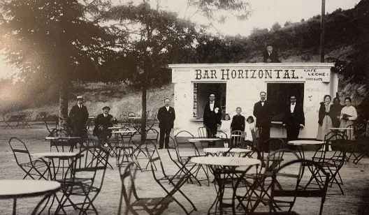 Fotografía antigua en sepia: el quiosco «Bar Horizontal» con mesas y sillas de hierro al aire libre, entre los árboles