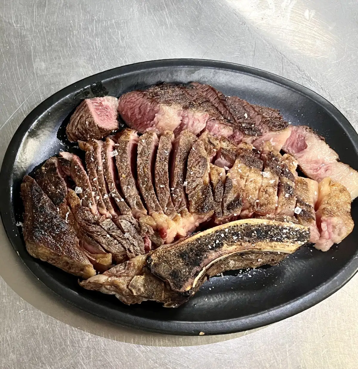 Chuletón de vaca a la brasa, cortado en lonchas sobre una fuente de hierro