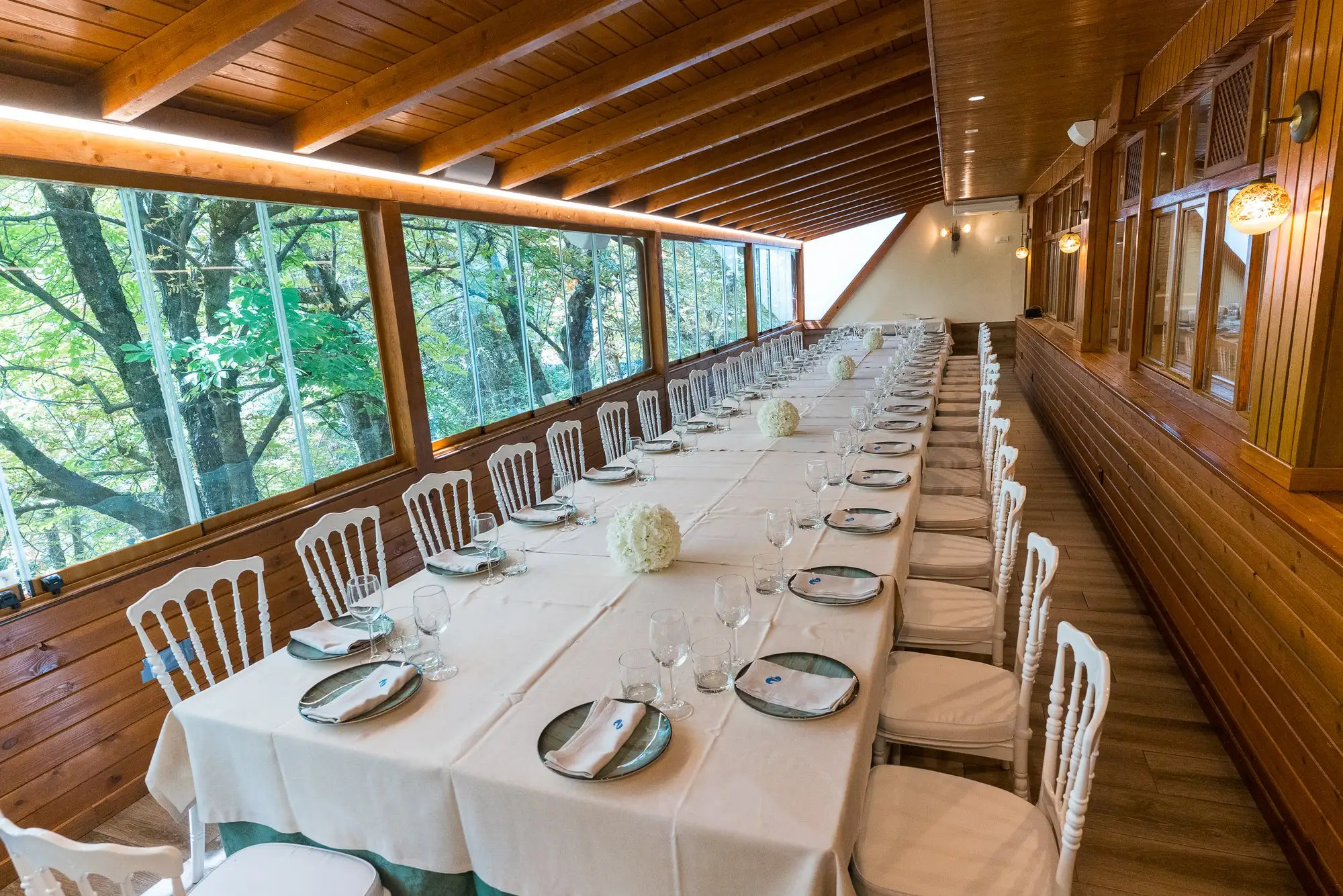 Mesa imperial montada para una celebración en el comedor acristalado, a lo largo de los ventanales y los árboles