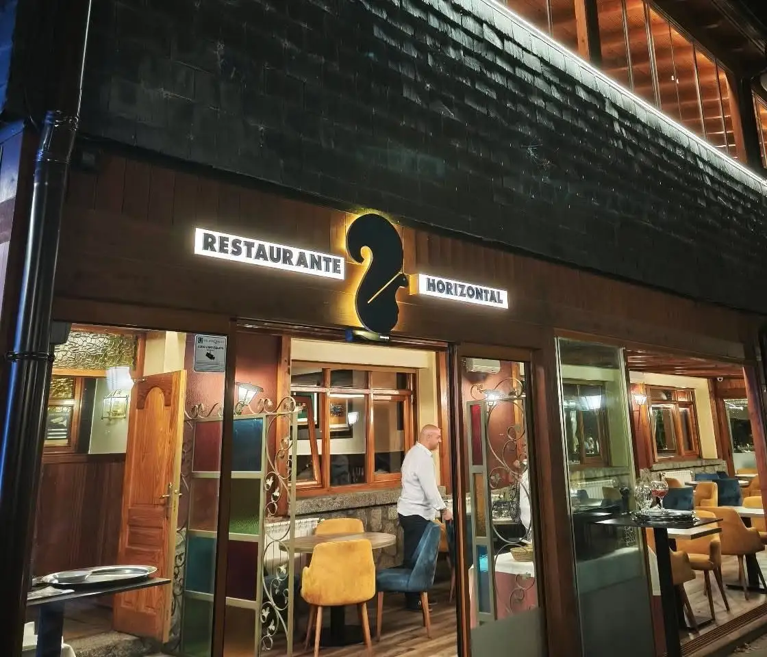 Fachada de Restaurante Horizontal de noche, con su rótulo iluminado y la ardilla, y el comedor encendido tras las puertas de cristal