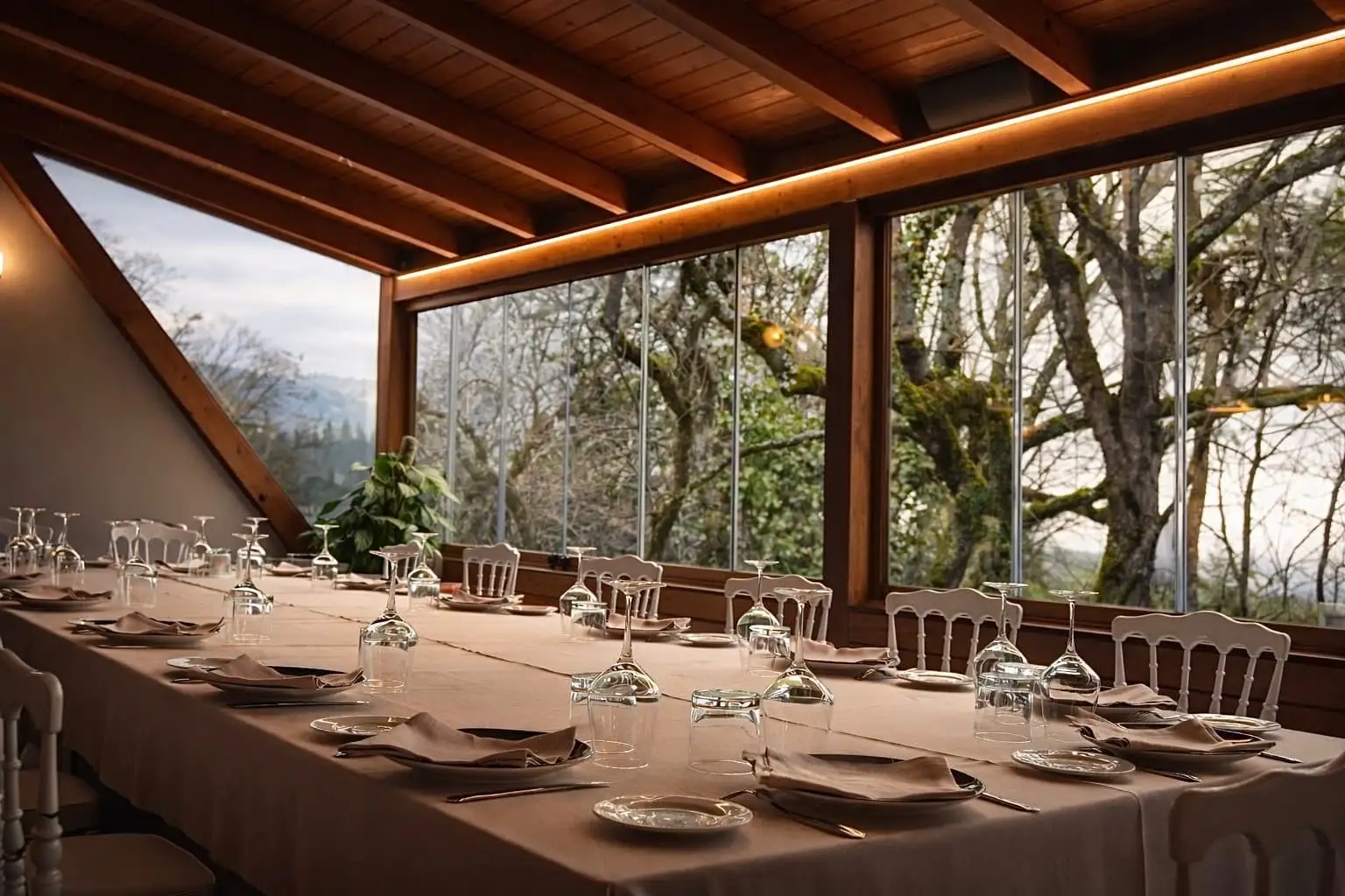 Mesa montada para una celebración en el comedor acristalado, con los árboles y la sierra al otro lado del cristal