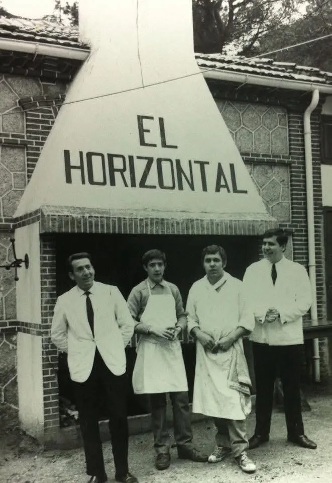 Fotografía antigua en blanco y negro: cuatro hombres con chaqueta o delantal blancos posan bajo la campana de la parrilla con el rótulo «El Horizontal»