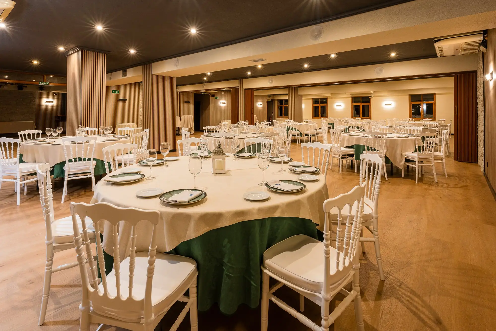 Mesa redonda montada para una celebración en el salón, con mantel verde y sillas blancas