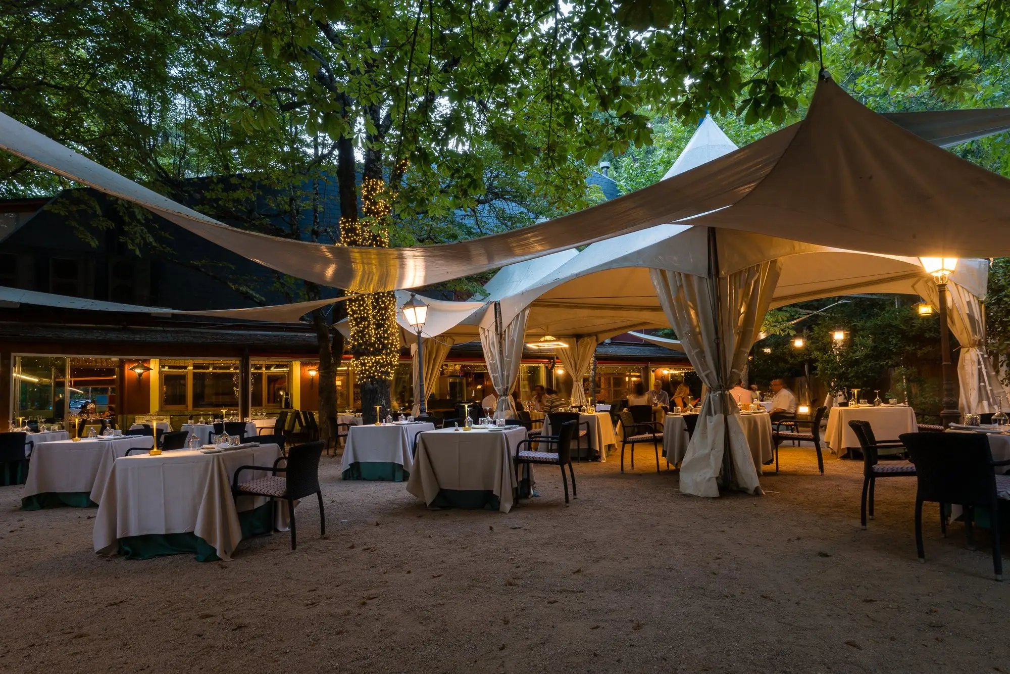 La terraza al anochecer, con las mesas vestidas bajo las carpas y los árboles iluminados