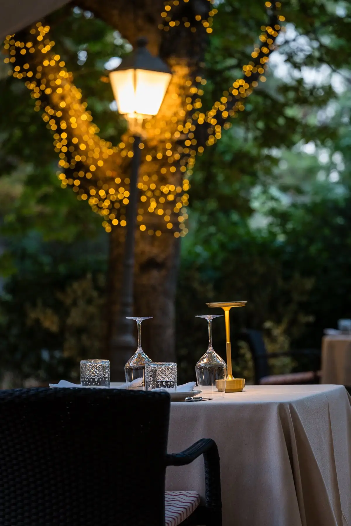 Una mesa de la terraza al anochecer, bajo un farol encendido y un árbol con guirnaldas de luces